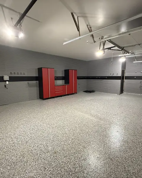 Two-car garage with red cabinets along the back wall, grey walls and a grey flake epoxy floor