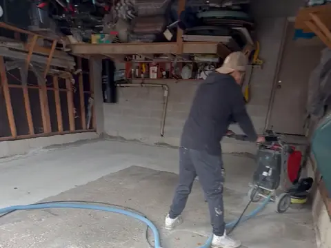 Grinding a bare concrete garage floor with a dust-extraction hose before coating
